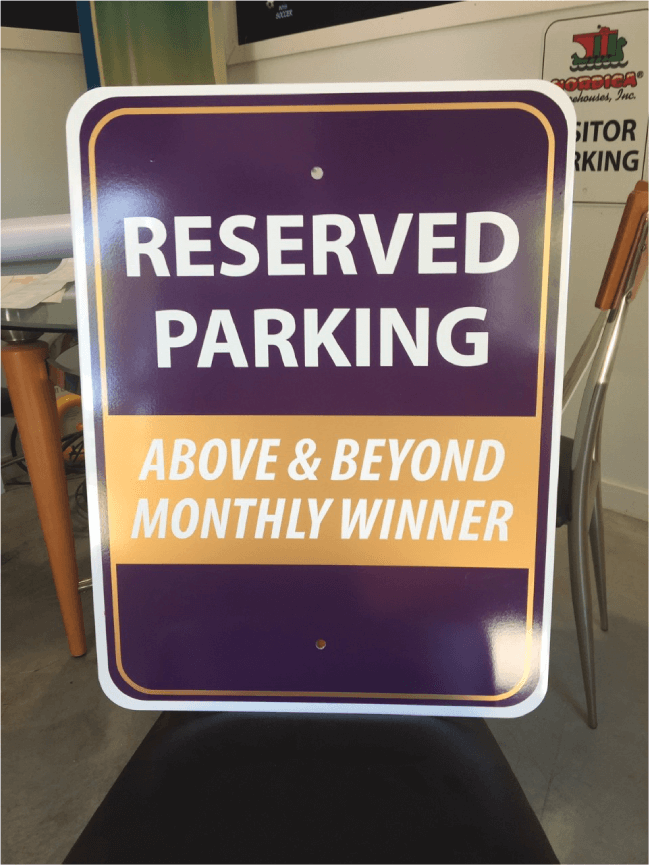 A purple and yellow sign that says reserved parking above & beyond monthly winner.